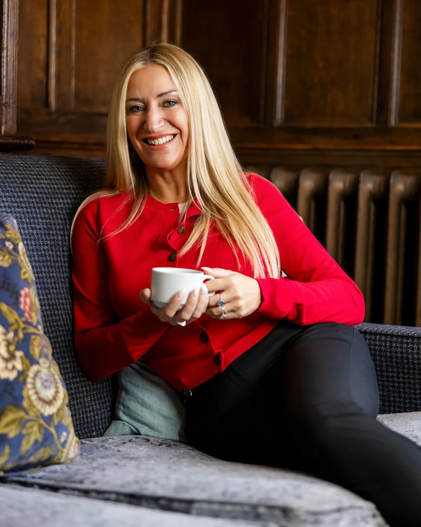 Gemma in a red cardigan, smiling with a cup of coffee at the Maids Head Hotel