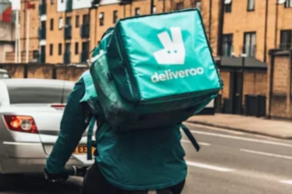 A Deliveroo rider carrying a delivery backpack, cycling on a city street