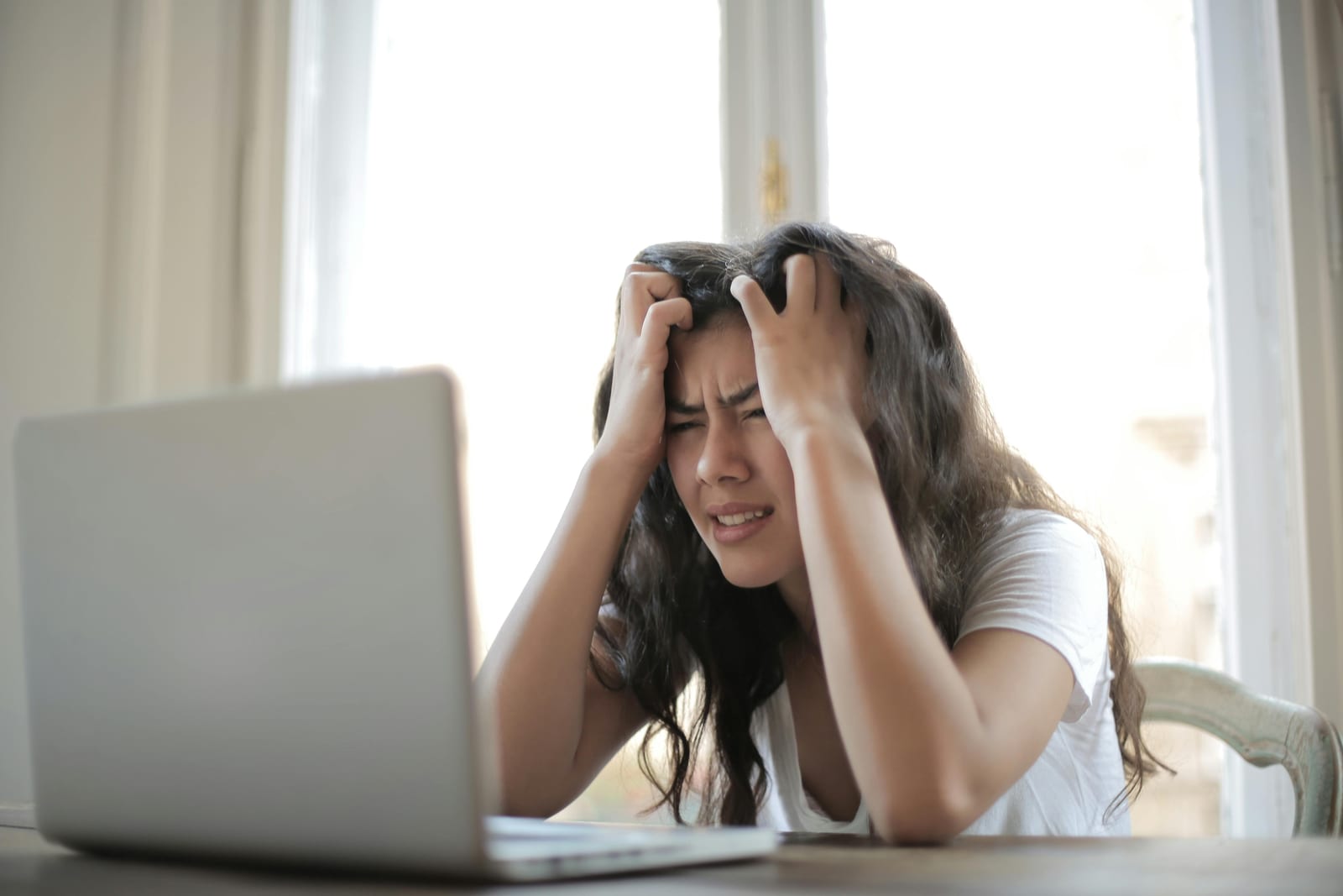 A woman at a laptop holding her head in frustration