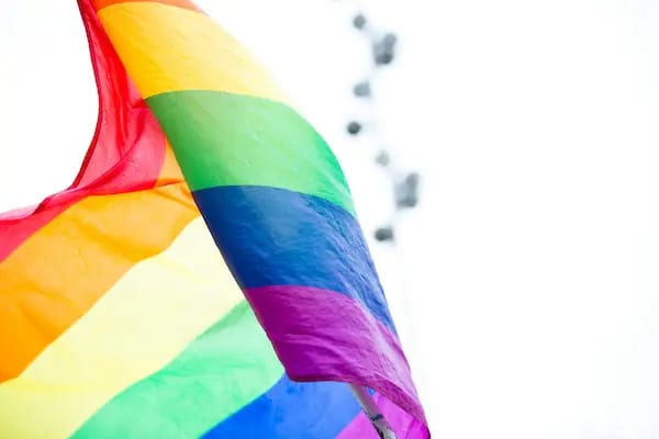 A rainbow Pride flag flying against a pale sky