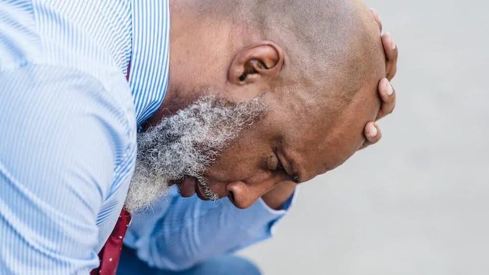 A man with his head bowed and his hand on his head, looking distressed