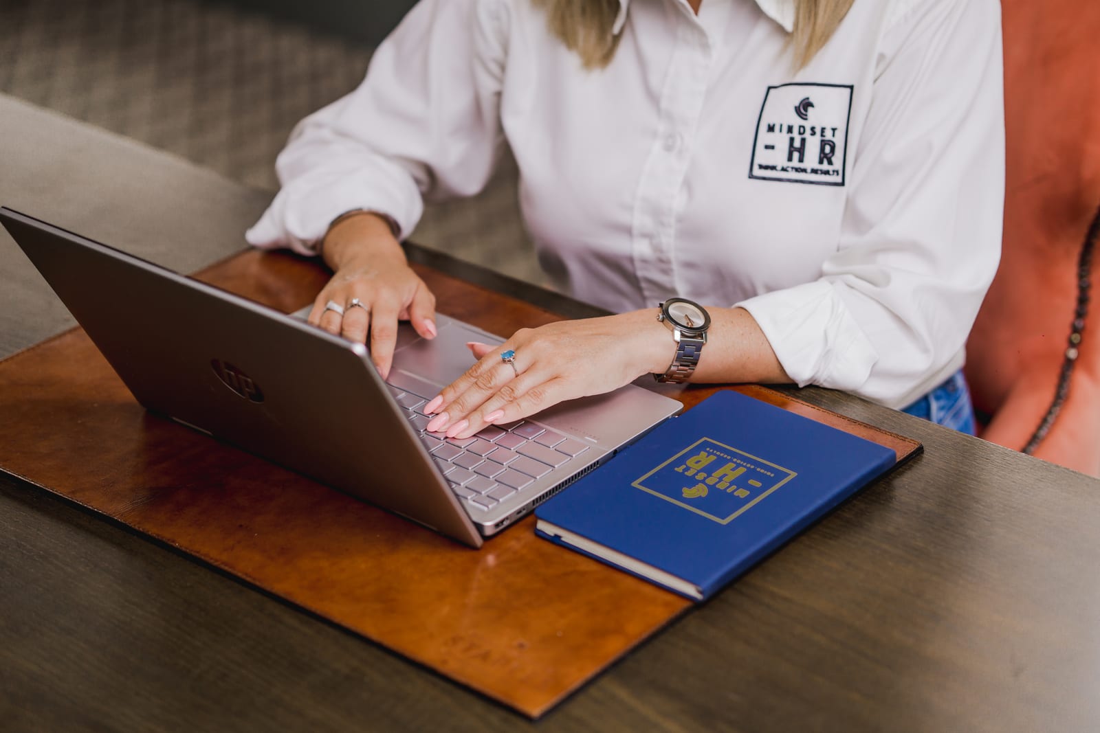 A Mindset HR consultant in a branded shirt working at a laptop beside a branded notebook